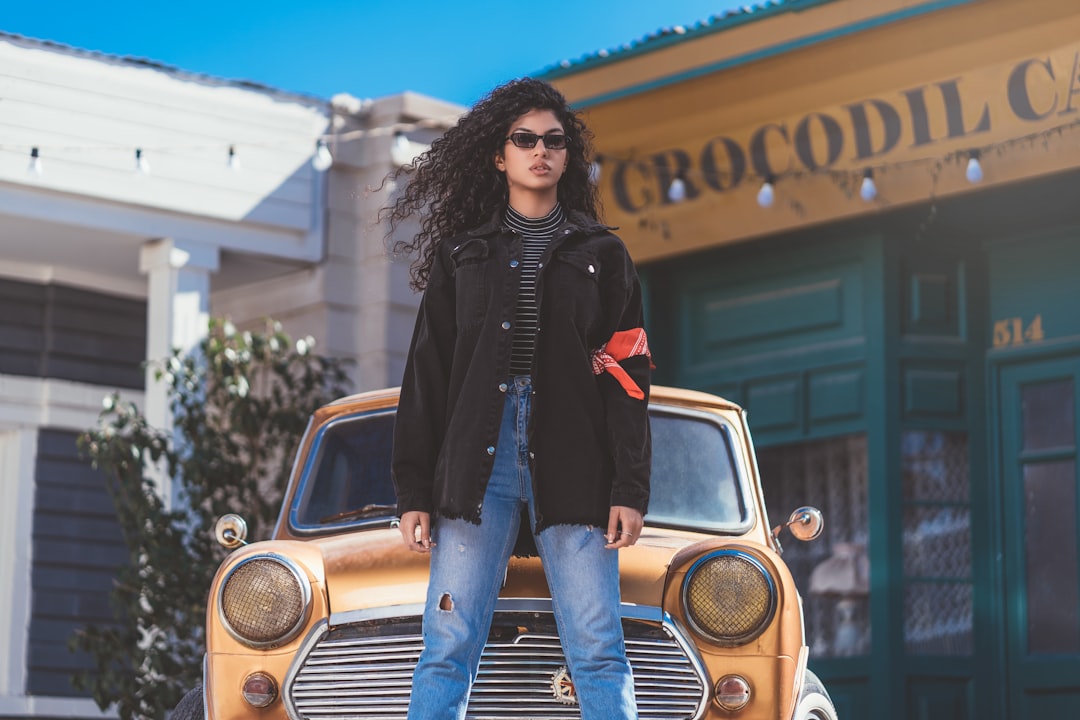 woman in black jacket and blue denim jeans standing beside yellow and silver vintage car during