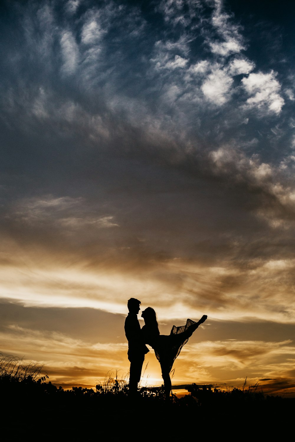 Siluetta dell'uomo e della donna che si baciano sotto il cielo nuvoloso durante il giorno