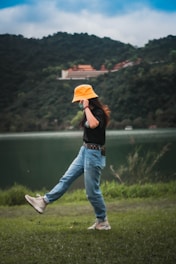 woman in red and white jacket and blue denim jeans holding orange and white surfboard
