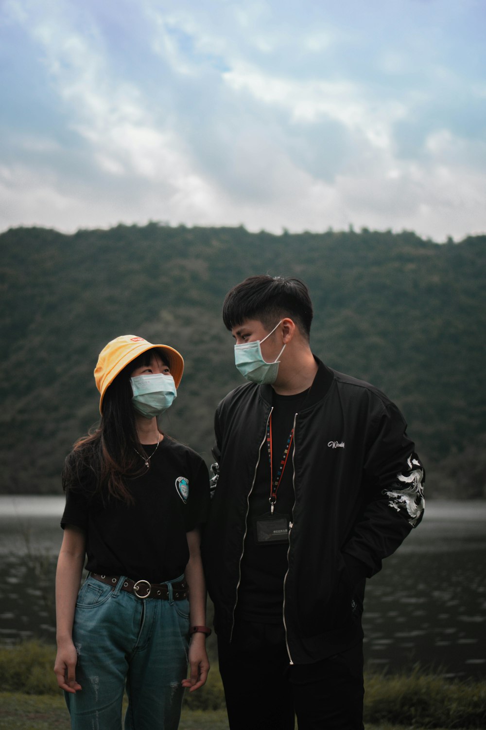 man in black jacket wearing orange cap and sunglasses standing beside woman in black jacket