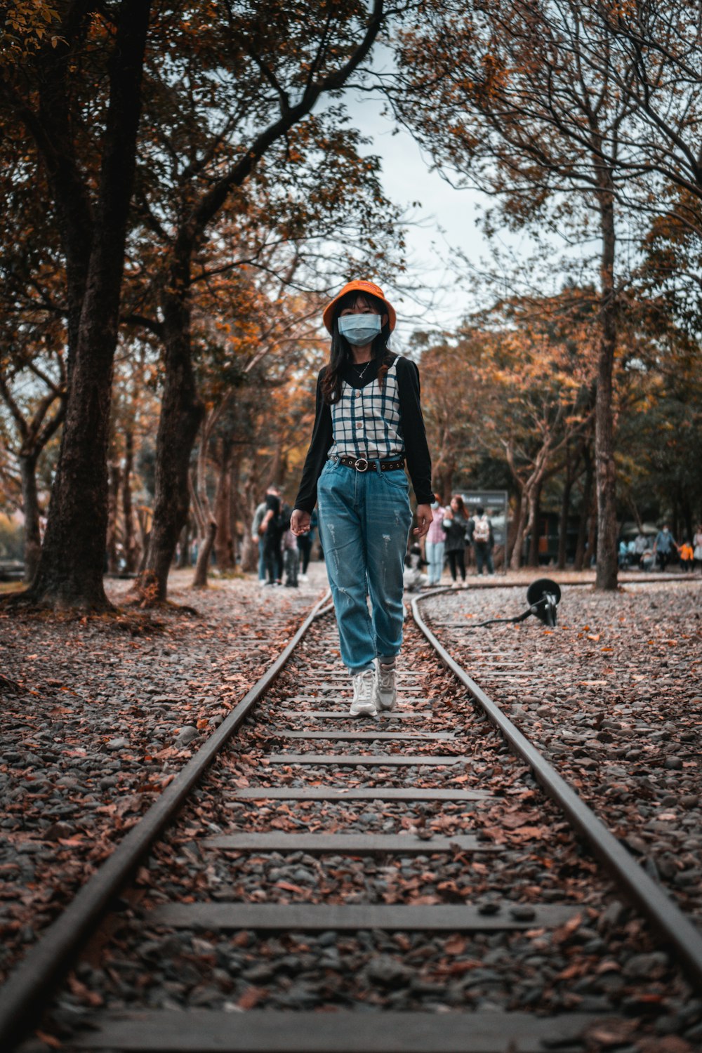 woman in black jacket and blue denim jeans standing on train rail during daytime
