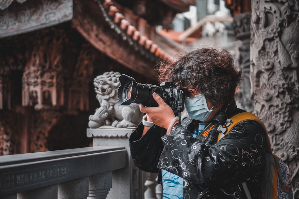 man in blue denim jacket holding black dslr camera