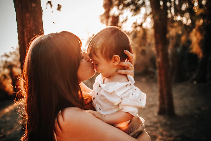Mãe beijando o bebê no colo sob a luz dourada do fim de tarde