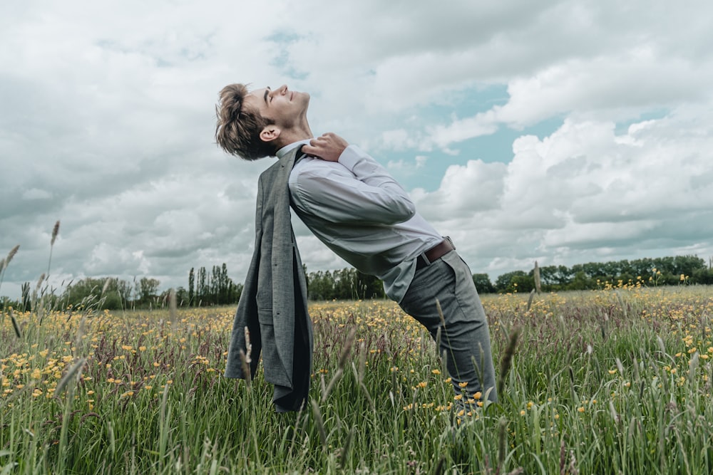 man in gray dress shirt and black pants standing on green grass field under white cloudy