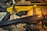 Two rifles are placed on a camouflage cloth surface. One rifle has a striking yellow finish, while the other is black. Scattered around them are several rifle cartridges and a pair of protective goggles.