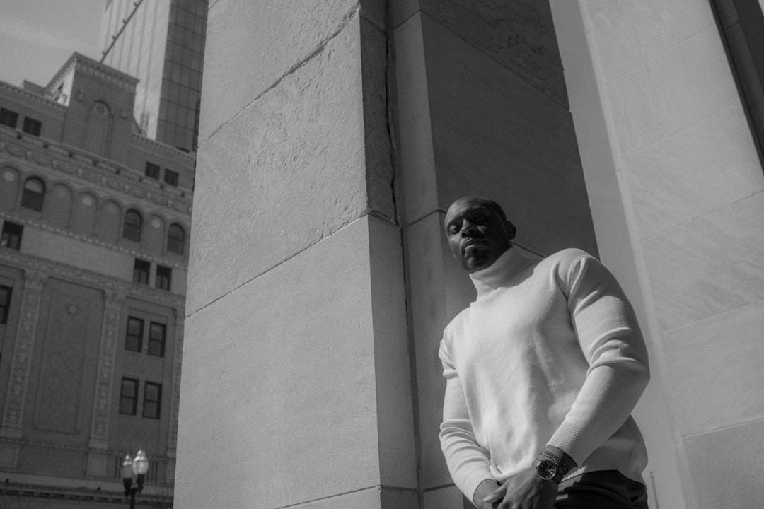 man in white long sleeve shirt and black pants sitting on concrete wall