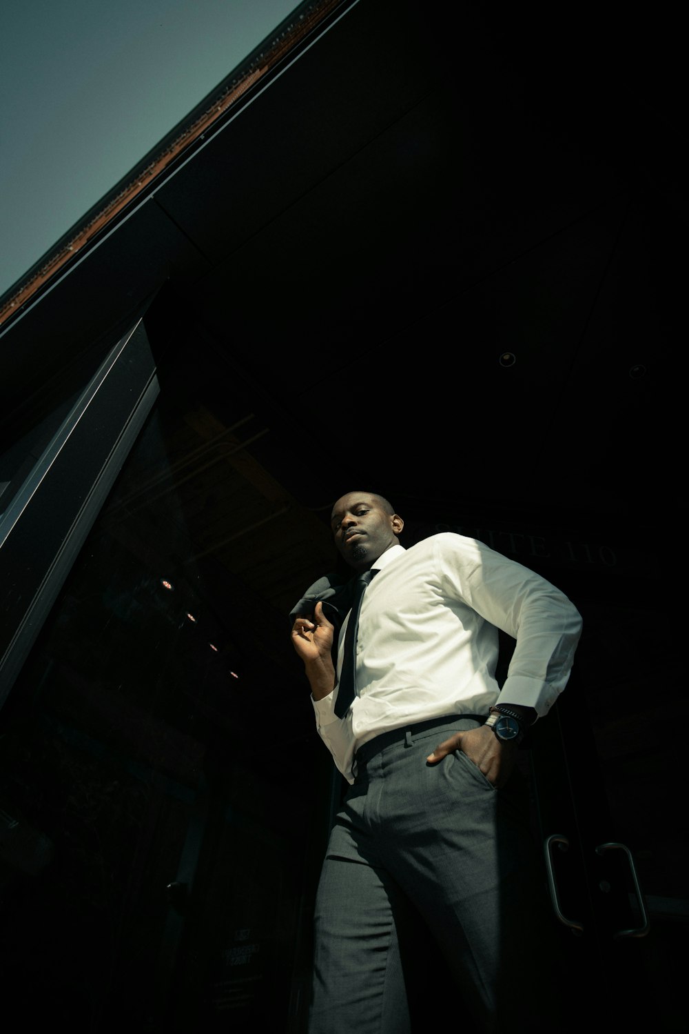 man in white dress shirt and black denim jeans standing beside black wall