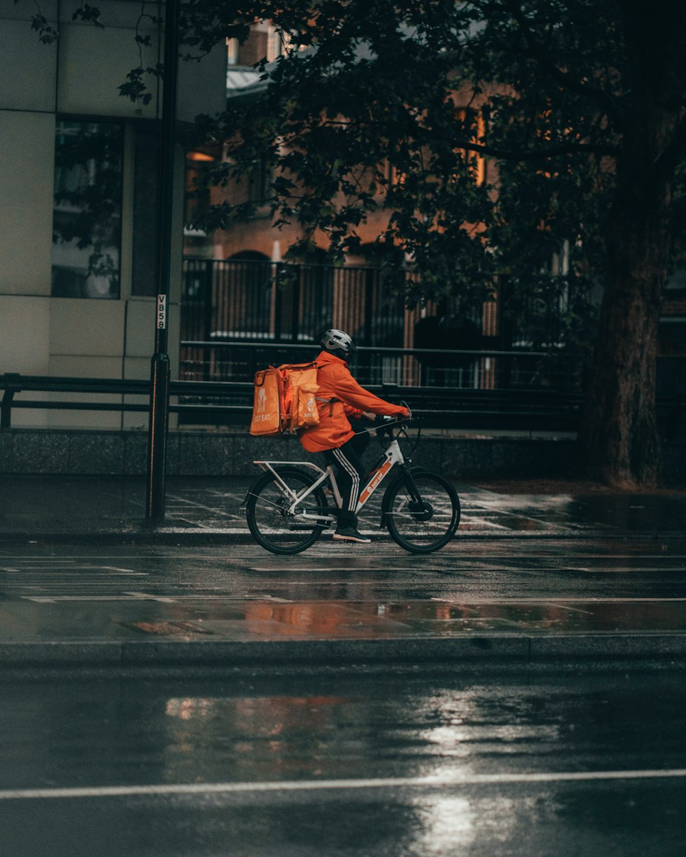 オレンジ色のジャケットを着た男性が夜間に路上で自転車に乗る