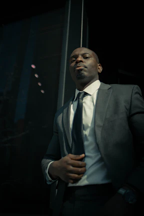 Formal wear with a model adjusting his black tie in front of a sleek, modern glass building.