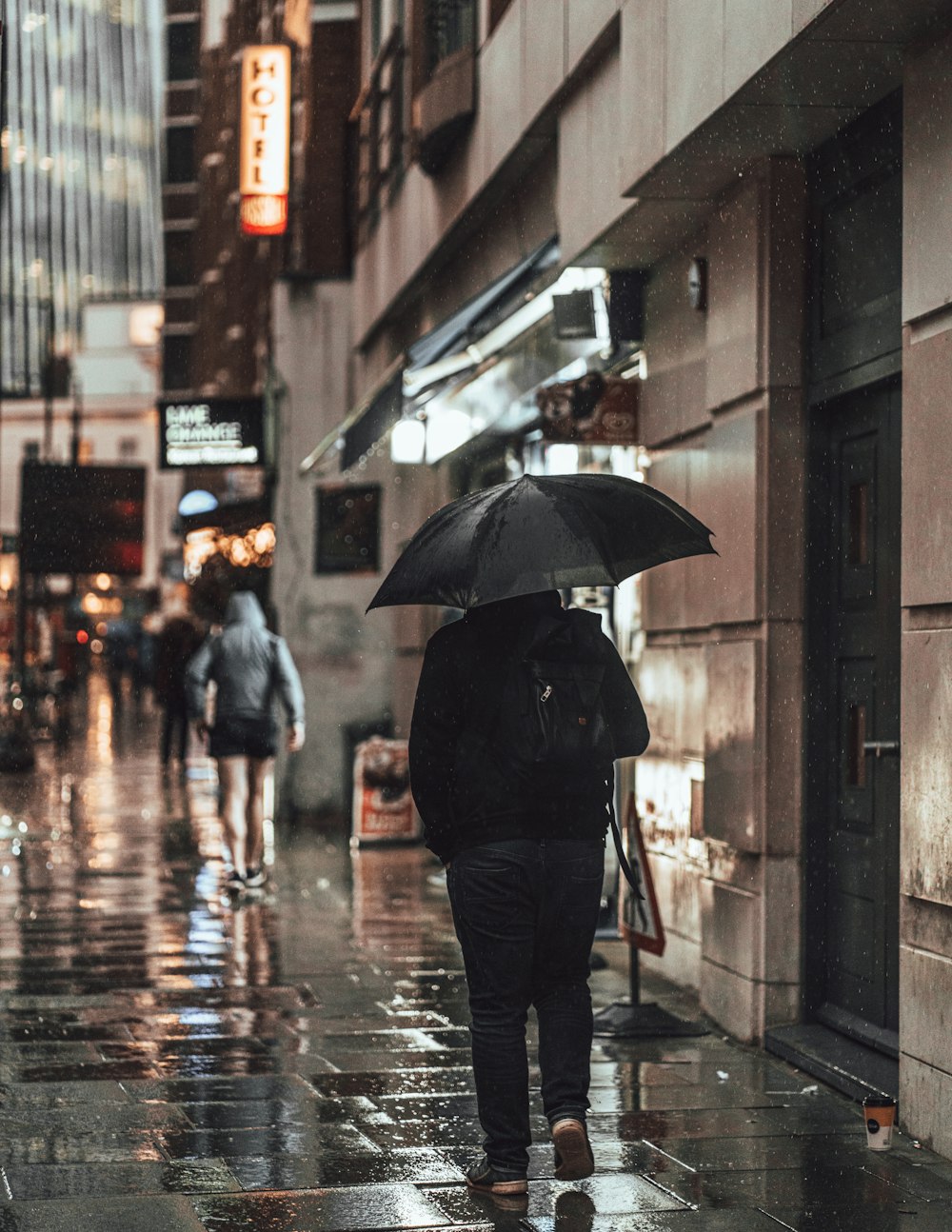 person in black jacket holding umbrella walking on sidewalk during daytime