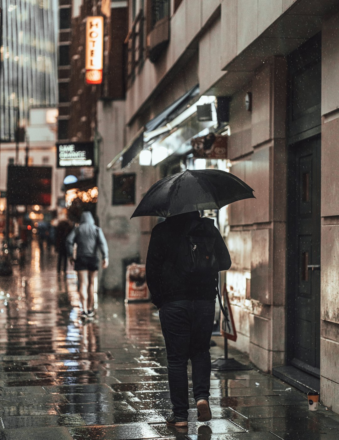 person in black jacket holding umbrella walking on sidewalk during daytime