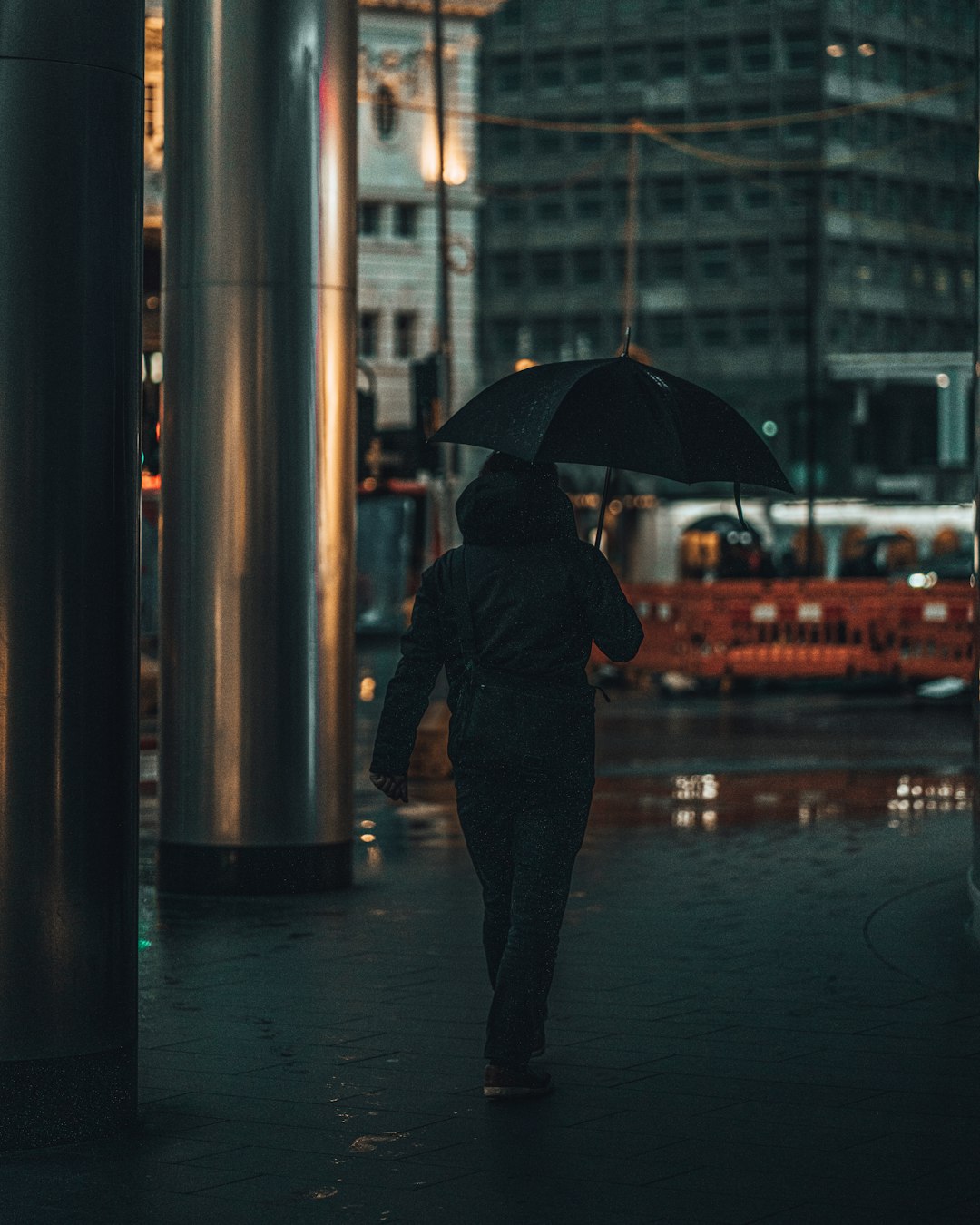 man in black jacket holding umbrella walking on sidewalk during night time