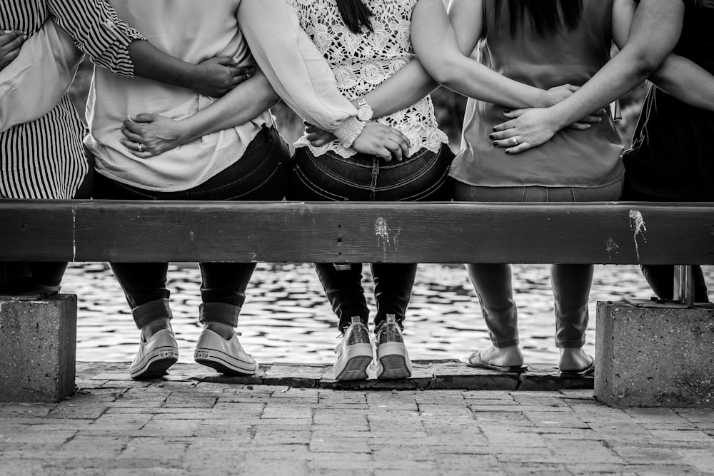 foto em tons de cinza de 3 mulheres sentadas no banco de madeira