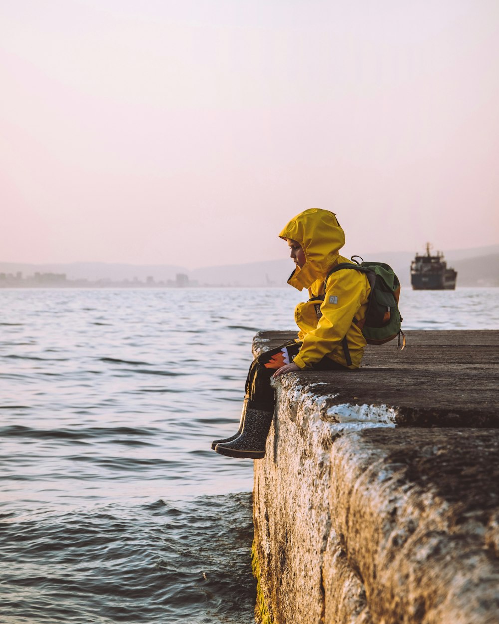 person in yellow hoodie sitting on brown wooden log in front of body of water during