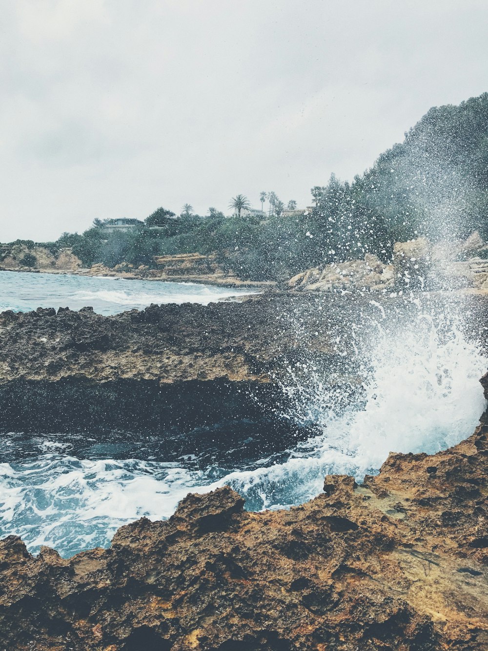 ocean waves crashing on brown rock formation under white cloudy sky during daytime