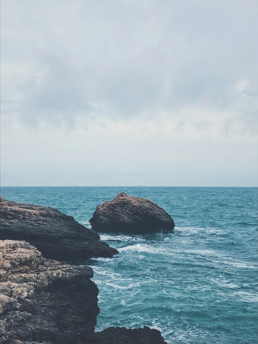 brown rock formation on sea under white clouds during daytime