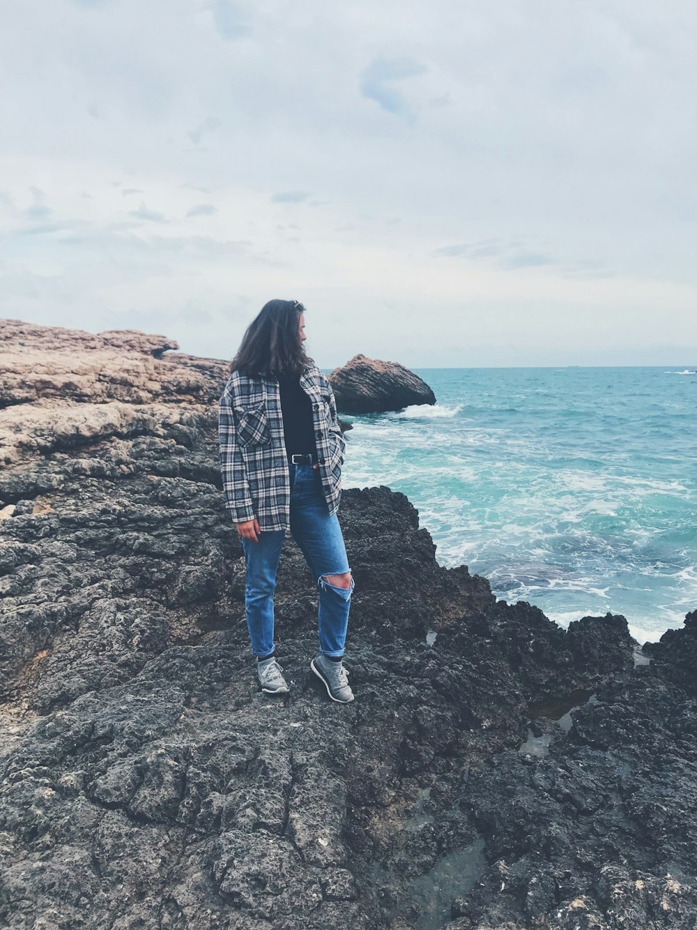 woman in black and white plaid long sleeve shirt and blue denim jeans standing on brown