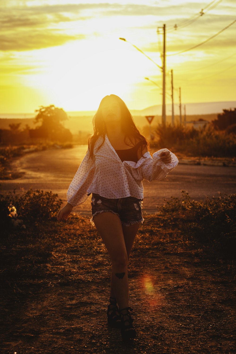 woman in white knit sweater and black denim daisy dukes walking on the field during sunset