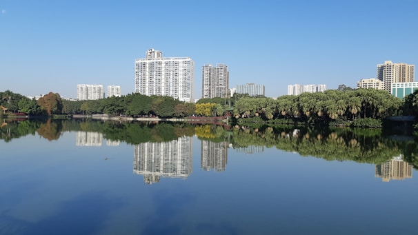 Elegant high-rise buildings of Ganga County reflecting in a serene water body under a clear blue sky.
