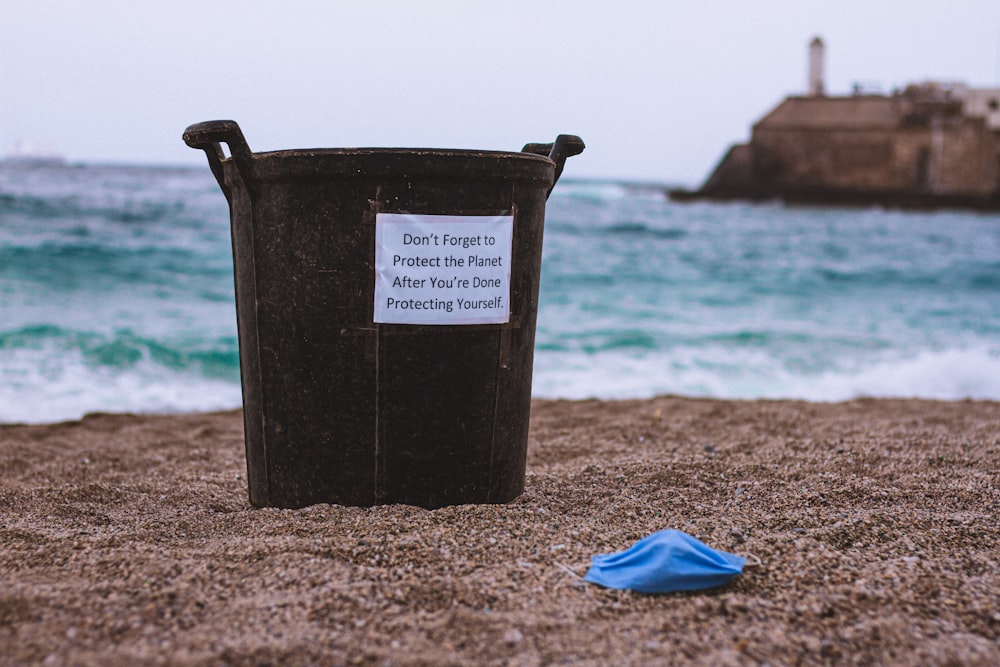 balde de plástico preto na areia marrom perto do tecido azul durante o dia