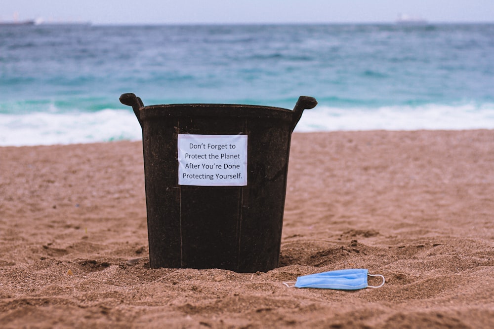 black plastic bucket on brown sand near blue and white plastic pack during daytime