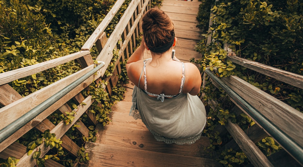 woman in white spaghetti strap top standing on brown wooden bridge during daytime