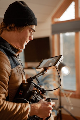 man in black knit cap and brown jacket using black laptop computer