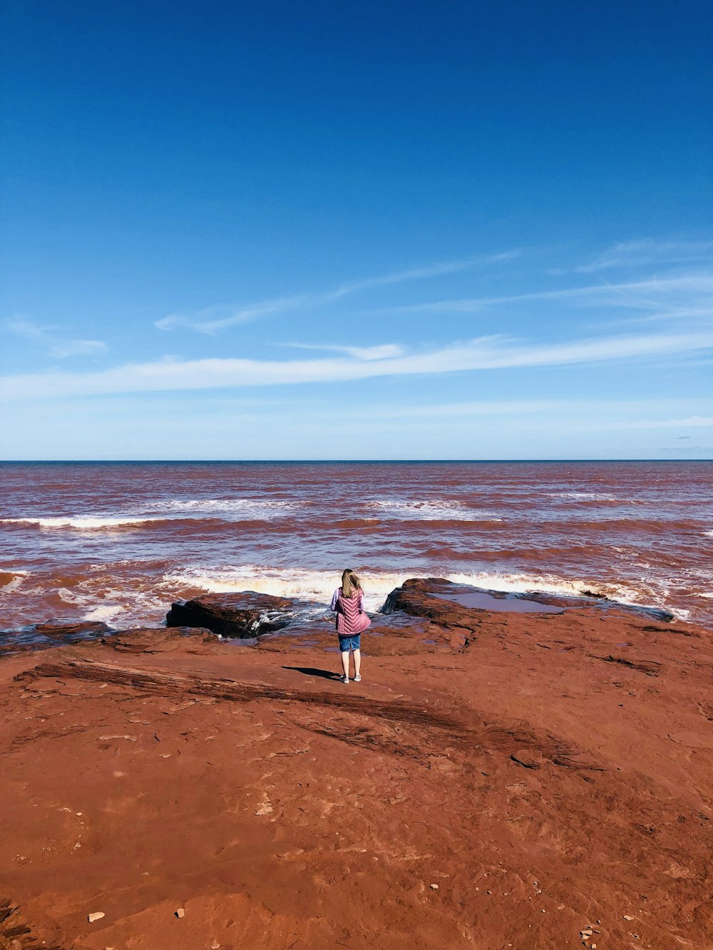 Mujer en vestido blanco de pie sobre arena marrón cerca del cuerpo de agua durante el día