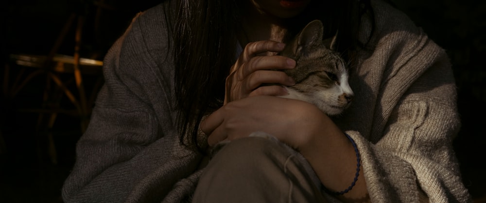 woman in gray long sleeve shirt holding brown tabby cat