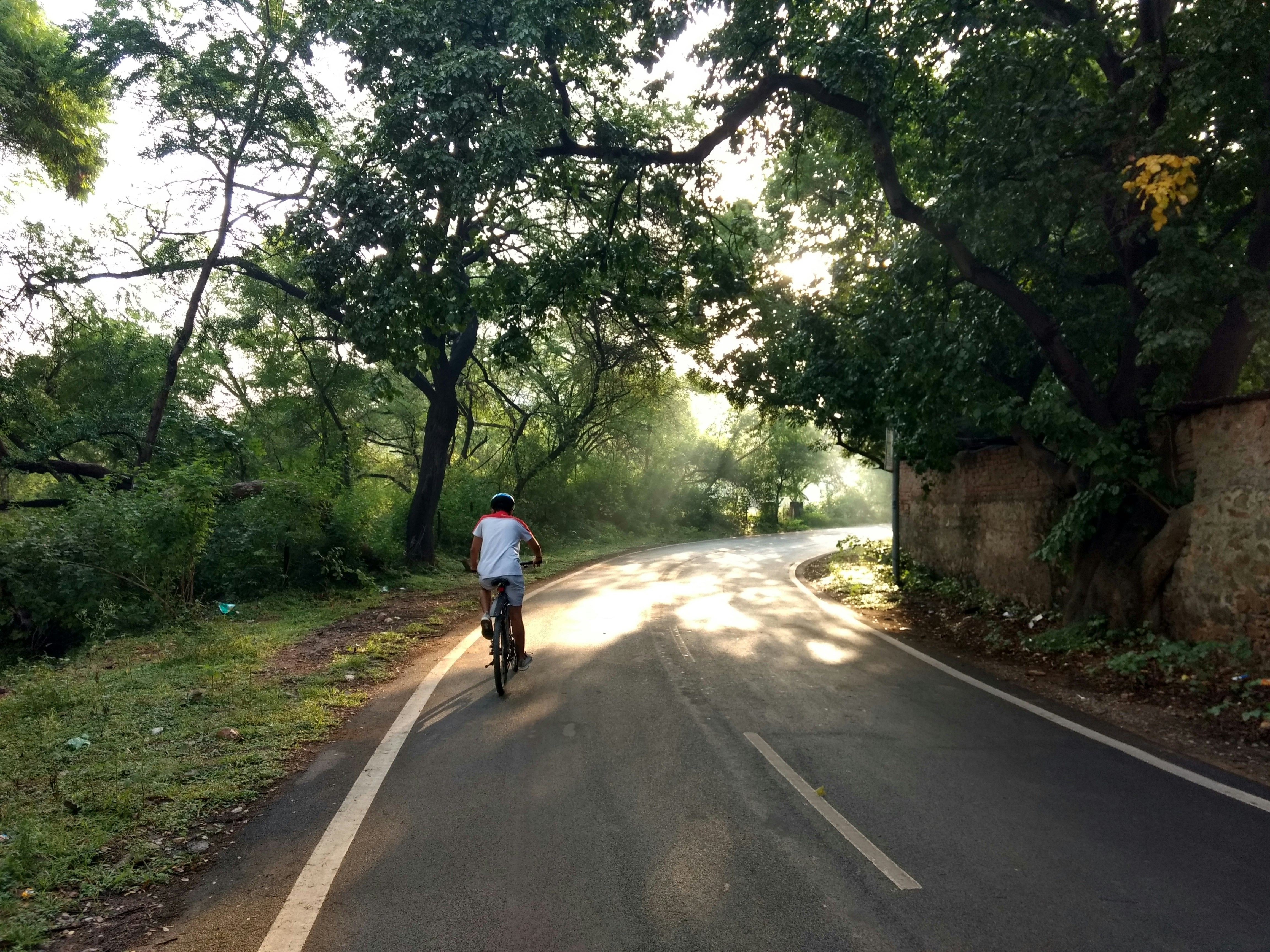 Man in white shirt riding bicycle on gray asphalt road during daytime ...