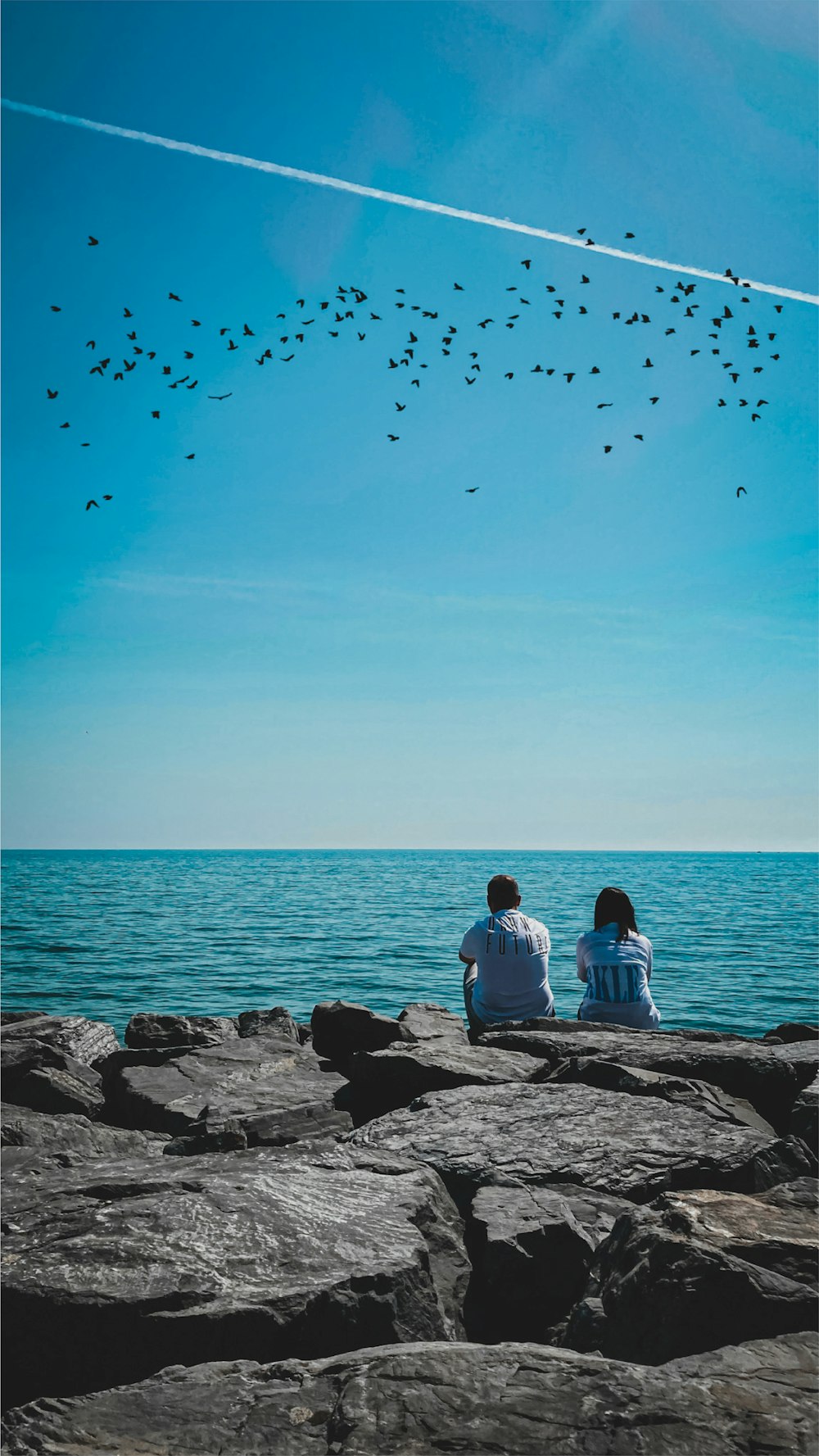man and woman sitting on rock near sea during daytime