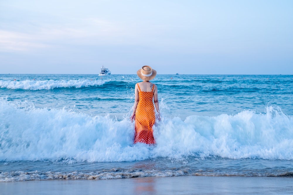 Mujer en vestido naranja de pie en la playa durante el día