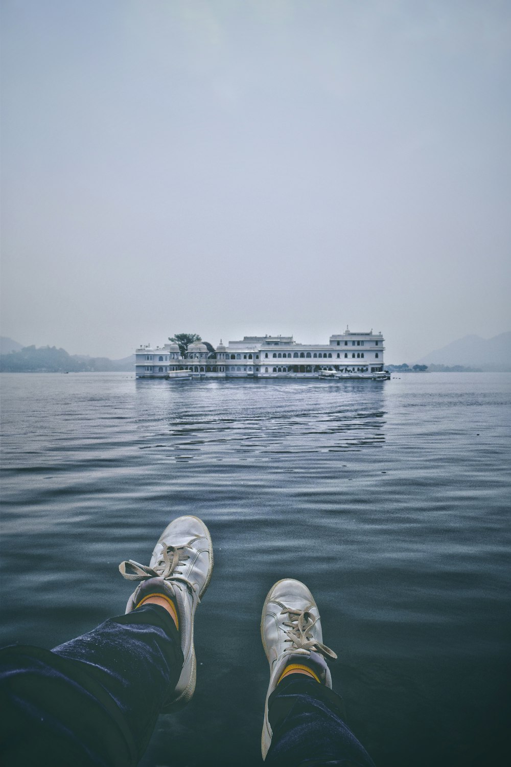 person in white and orange sneakers sitting on white and blue boat on sea during daytime