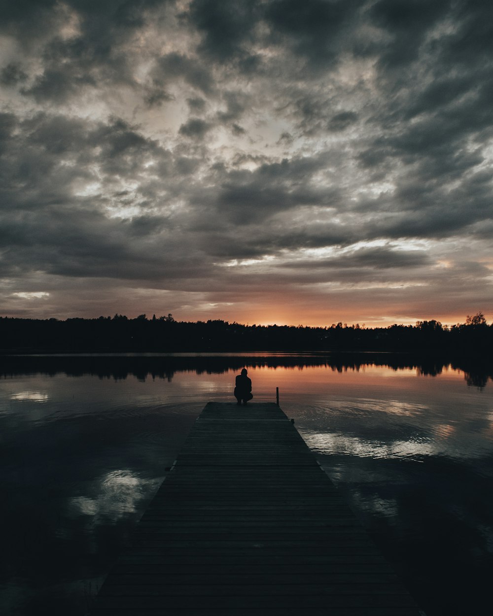 Person, die während des Sonnenuntergangs auf dem Dock sitzt