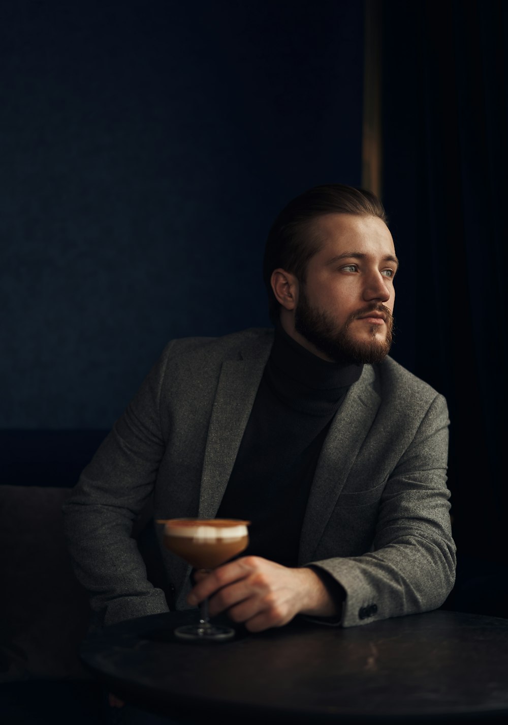 man in gray suit jacket holding brown ceramic mug