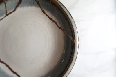 Close-up of hands delicately repairing a cracked ceramic bowl with gold lacquer.