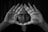 A person looks through a triangle formed by their hands, creating a focused and intense gaze. The image is in black and white, enhancing the dramatic and introspective mood.