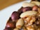 A close-up view of various types of nuts embedded in a baked item. The image features whole almonds and hazelnuts with a glossy, roasted appearance set against a textured brown surface.
