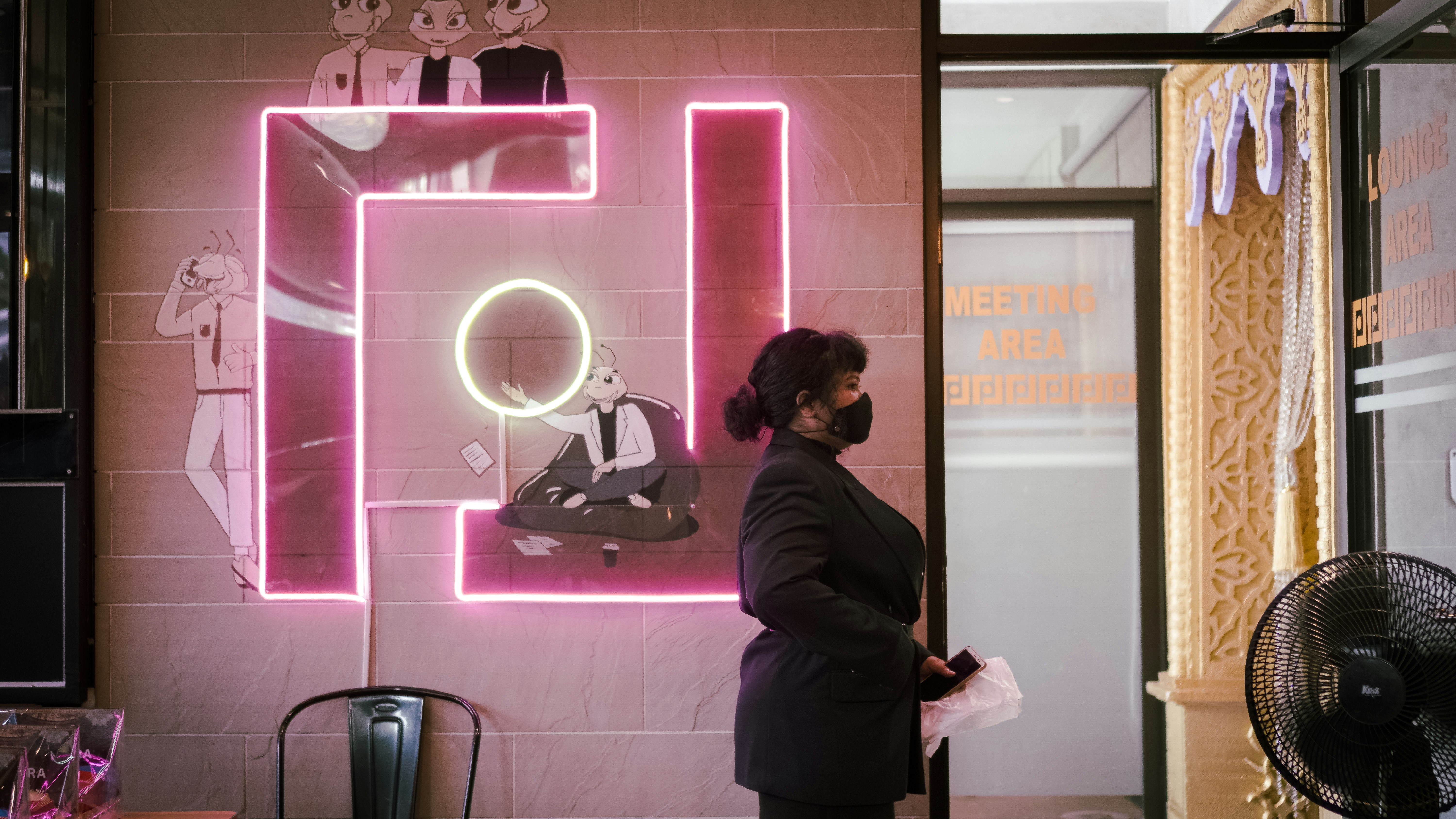 woman in black coat standing in front of pink and white wall
