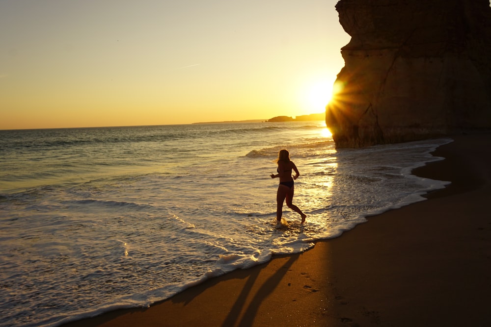 woman in black bikini walking on beach during sunset