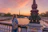 A smiling woman standing on a Paris balcony overlooking the Eiffel Tower at sunset.