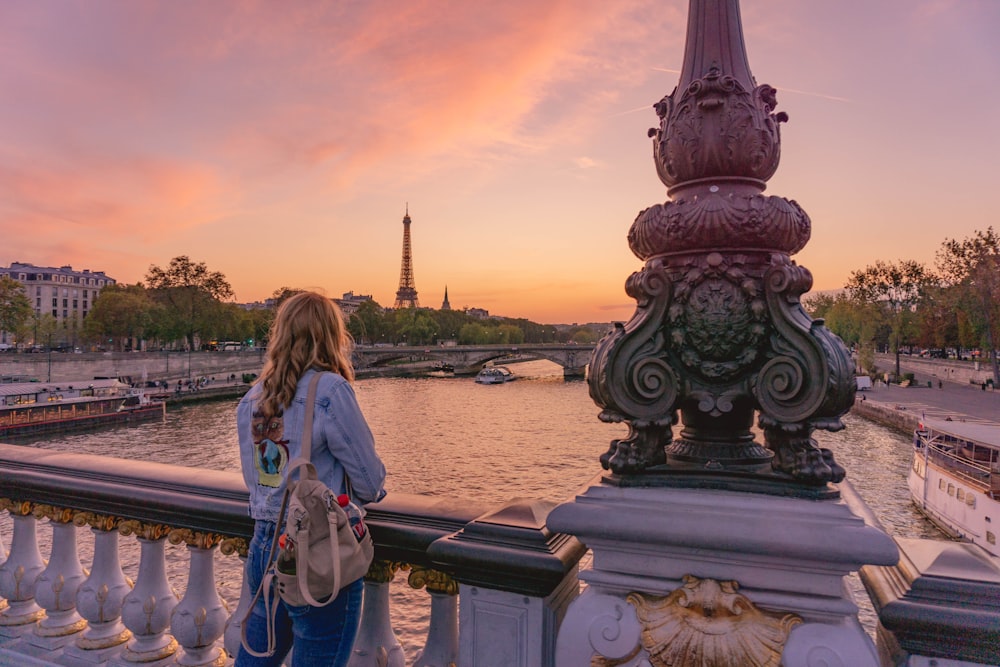 woman in blue and white dress standing on gray concrete bridge during sunset