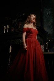 A poised woman in a flowing champagne gown stands against a marble backdrop, embodying elegance and artistic confidence.