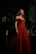 A silhouette of a woman draped in a deep burgundy velvet robe against a dark backdrop.