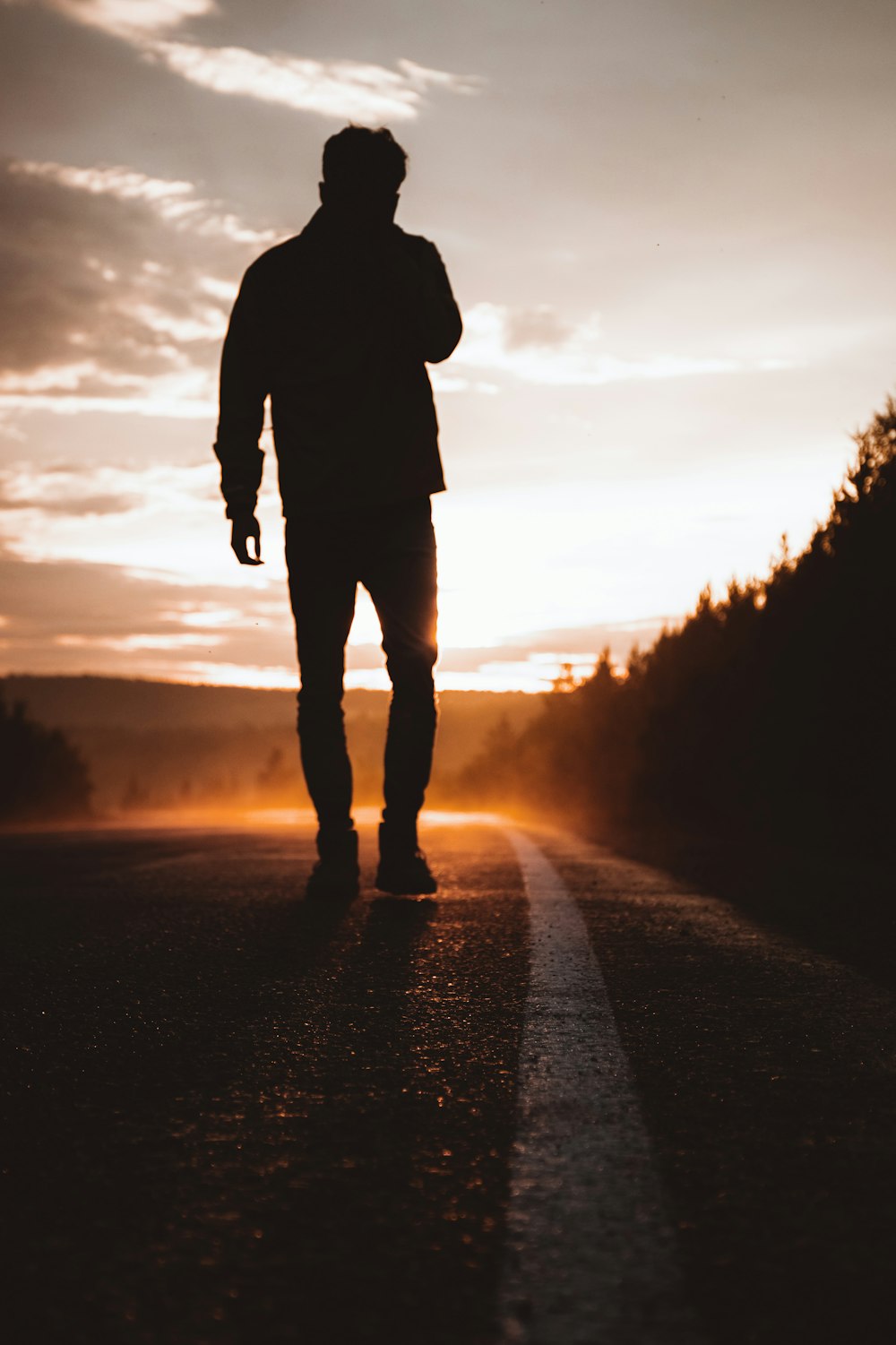 silhouette of person standing on road during sunset