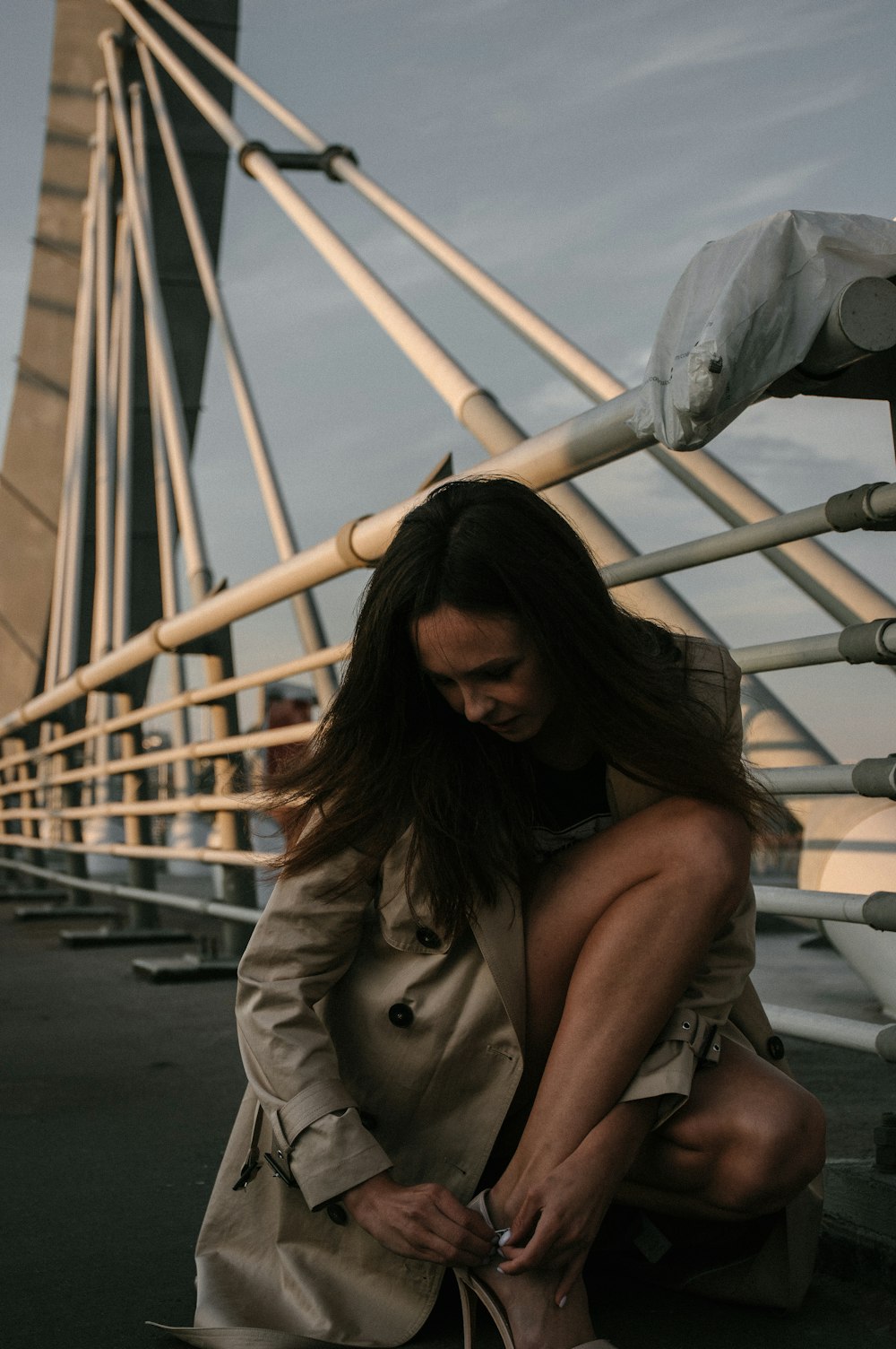 woman in brown coat sitting on white metal railings during daytime