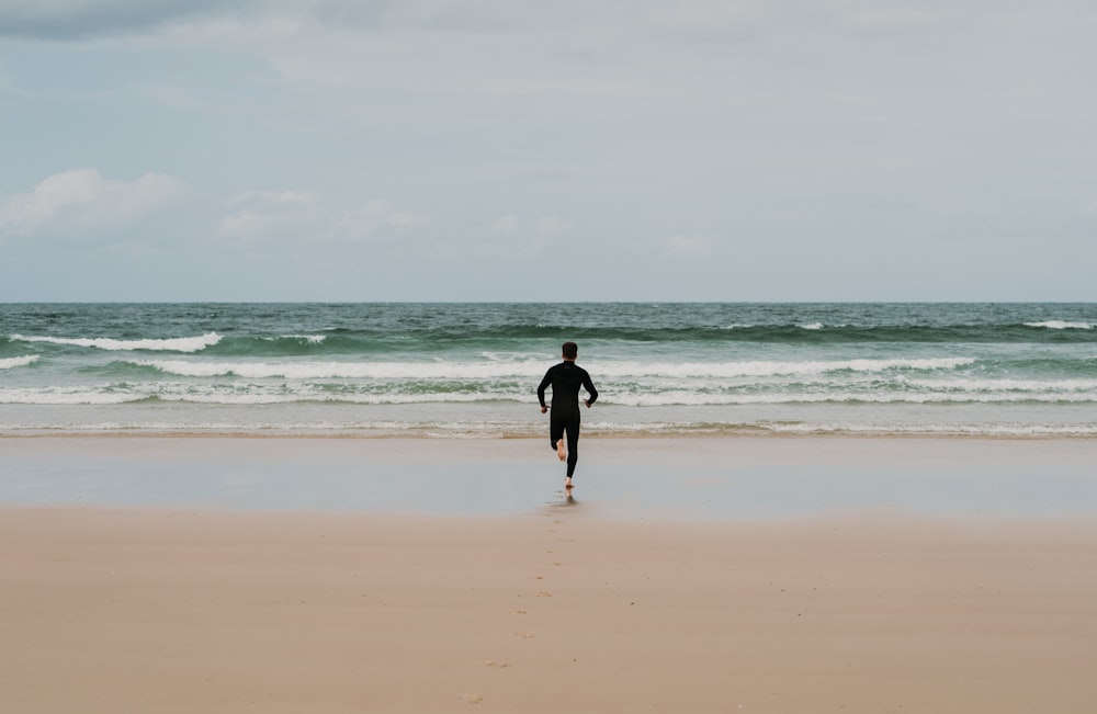 homem na camisa preta andando na praia durante o dia