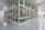 An empty industrial warehouse with metal shelves organized in rows. The polished gray floor reflects the overhead fluorescent lighting. The shelves are sturdy, with yellow guards and identification labels. The environment appears clean and spacious.