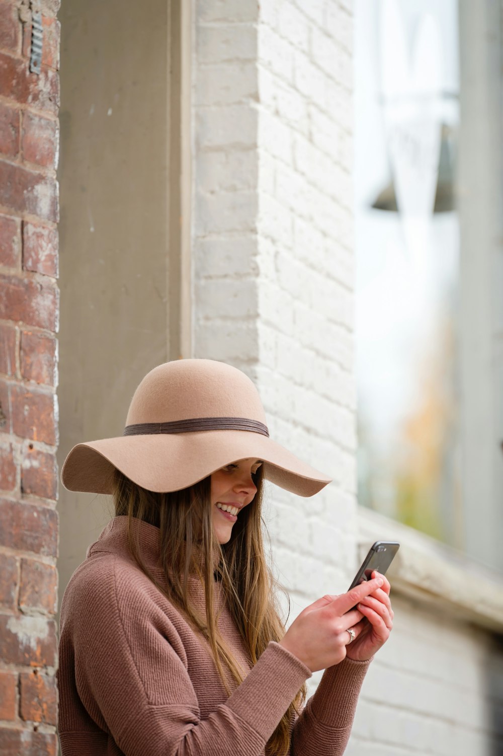 Mujer con sombrero marrón y suéter marrón sosteniendo un teléfono inteligente