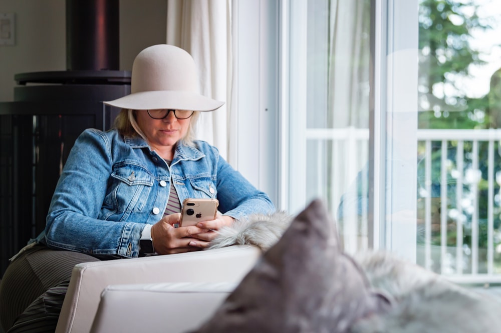 woman in blue denim jacket and gray hat sitting on white chair